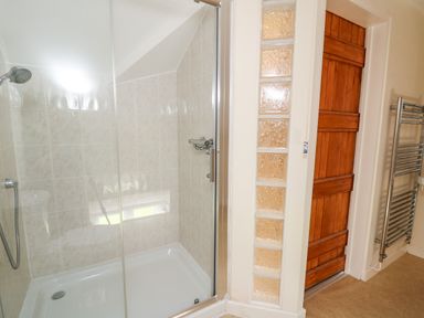A bathroom with a glass enclosed shower next to a wooden door and a heated towel rail at Railway Station Cottage in New Radnor near Kington