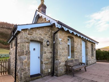 An exterior view of a stone cottage with blue doors a wooden bench and a chimney at Railway Station Cottage in New Radnor near Kington