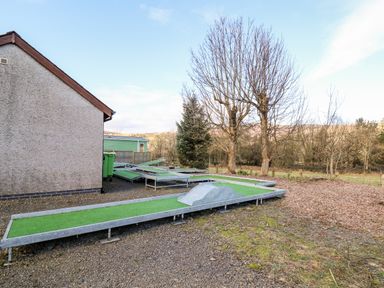 An outdoor mini golf course with artificial turf next to a building with leafless trees in the background at Railway Station Cottage in New Radnor near Kington