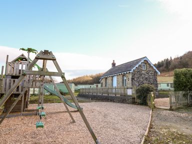 An outdoor playground with swings and slide next to a stone cottage and mobile homes at Railway Station Cottage in New Radnor near Kington