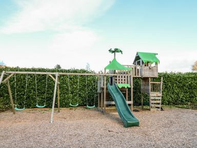 An outdoor playground with swings slide and climbing structure surrounded by hedges at Railway Station Cottage in New Radnor near Kington