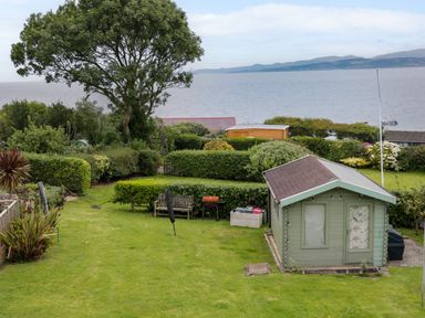 A garden with a small shed a bench and a barbecue overlooking the sea at 3 Moranedd in Moelfre