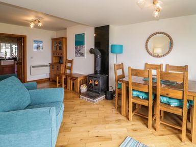 A living room with a blue sofa wooden dining table with chairs and a wood burning stove at 3 Moranedd in Moelfre