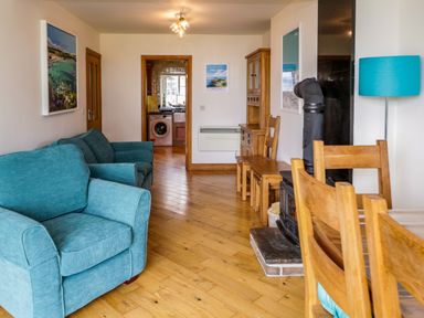 A living room with blue armchairs wooden furniture and a wood stove at 3 Moranedd in Moelfre
