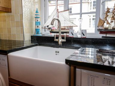 A kitchen sink with a silver faucet near a window with model ships ceramic cups and a lighthouse decoration at 3 Moranedd in Moelfre