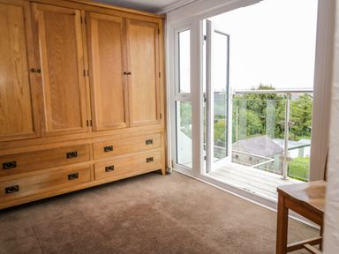 A room with wooden built-in cupboards a wooden chair an open glass door leading to a balcony with glass railing at 3 Moranedd in Moelfre