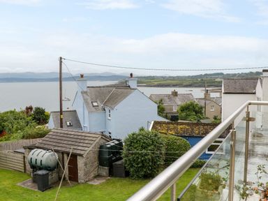 A coastal view with houses trees and a small shed beside a glass balcony at 3 Moranedd in Moelfre