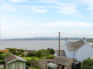 A coastal view with houses gardens and a body of water with hills in the background at 3 Moranedd in Moelfre