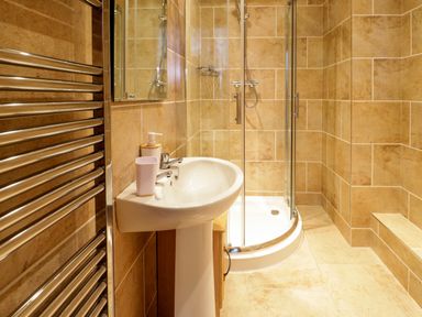A bathroom with a pedestal sink a glass shower enclosure and a chrome towel radiator at 3 Moranedd in Moelfre