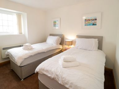 A bedroom with two single beds with white bedding and towels on each bed a bedside table with a lamp and framed pictures on the wall at 3 Moranedd in Moelfre