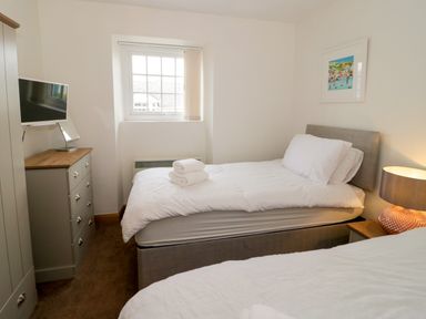 A bedroom with two single beds white bedding a chest of drawers with a TV and a window at 3 Moranedd in Moelfre