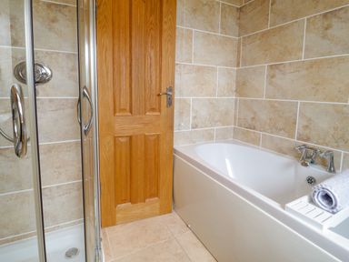 A bathroom with a bathtub a shower enclosure and a wooden door at 3 Moranedd in Moelfre