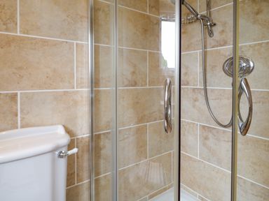 A shower enclosure with glass doors and chrome handles next to a white toilet tank in a tiled bathroom at 3 Moranedd in Moelfre