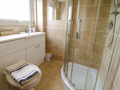 A bathroom with a shower enclosure a white cabinet a toilet with folded towels and a window at 3 Moranedd in Moelfre