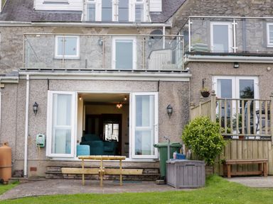 Backyard with wooden bench outside a house with open double doors and balconies at 3 Moranedd in Moelfre