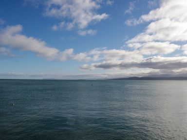 A large body of water under a blue sky with scattered clouds and distant land visible on the horizon at 3 Moranedd in Moelfre