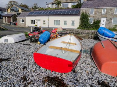 Small boats and fishing equipment on a pebble beach in front of houses with solar panels at 3 Moranedd in Moelfre