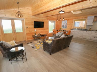 A living room with wooden walls a television a sofa and chairs a dining table and kitchen at Height End Farm Log Cabin Rossendale near Bacup