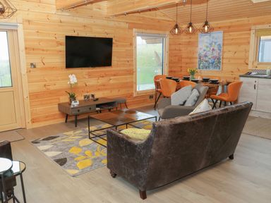 A living area with a wall-mounted TV a coffee table and seating next to a dining table with orange chairs at Height End Farm Log Cabin Rossendale near Bacup