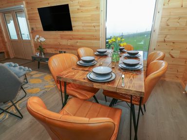 A dining area with a wooden table set with six place settings and orange chairs at Height End Farm Log Cabin Rossendale near Bacup