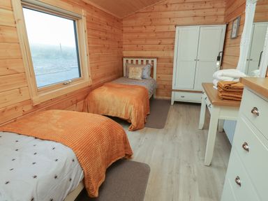 A bedroom with two single beds wooden walls a white wardrobe and a dresser at Height End Farm Log Cabin Rossendale near Bacup