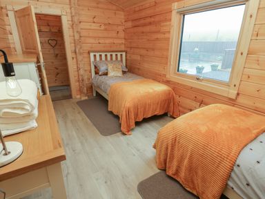 A bedroom with two single beds with orange blankets and a window at Height End Farm Log Cabin Rossendale near Bacup