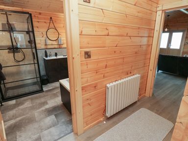 A hallway with wooden walls leading to a bathroom with a glass shower and a living room at Height End Farm Log Cabin Rossendale near Bacup