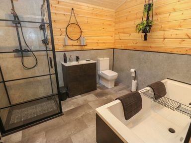 A bathroom with a shower, bathtub, sink, toilet, and wooden panel walls at Height End Farm Log Cabin Rossendale near Bacup