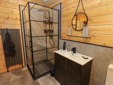 A bathroom with a glass shower enclosure a sink cabinet with a mirror above and a towel hanging on a radiator at Height End Farm Log Cabin Rossendale near Bacup