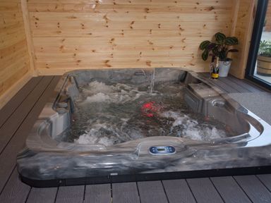 An indoor hot tub with water jets and bubbles in a wooden room with a plant and champagne bottles at Height End Farm Log Cabin Rossendale near Bacup