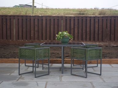 An outdoor patio with a glass table and four green chairs with a potted plant on the table at Height End Farm Log Cabin in Rossendale near Bacup