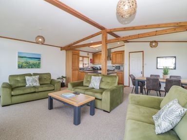 A living room with green sofas, a wooden coffee table, and a dining table with chairs at Three Views Lodge in Whitsand Bay Fort Holiday Village