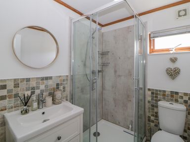 A bathroom with a shower enclosure sink with toiletries circular mirror and a toilet at Three Views Lodge in Whitsand Bay Fort Holiday Village