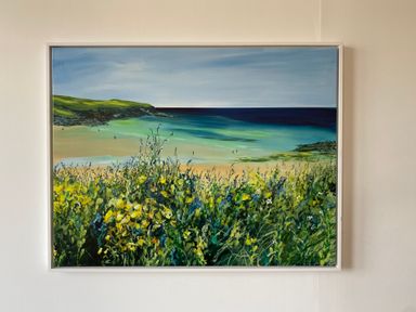 A framed painting of a coastal scene with wildflowers in the foreground and a beach with cliffs and ocean in the background at Three Views Lodge in Whitsand Bay Fort Holiday Village