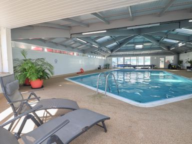 An indoor swimming pool with deck chairs and plants at Three Views Lodge Whitsand Bay Fort Holiday Village