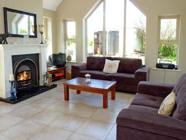 A living room with two sofas a wooden coffee table a fireplace and a television at Bluebell Cottage in Spanish Point County Clare