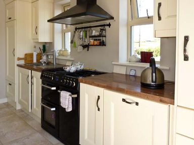 A kitchen with cream cabinets a black stove wooden countertops and windows at Bluebell Cottage in Spanish Point County Clare