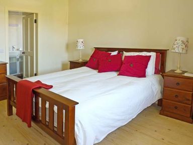 A bedroom with a wooden bed with white bedding and red pillows flanked by wooden nightstands with lamps at Bluebell Cottage Spanish Point County Clare