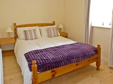 A bedroom with a wooden bed a purple blanket striped pillows wooden bedside tables and lamps at Bluebell Cottage in Spanish Point County Clare