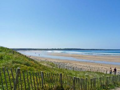A sandy beach with waves and a grassy dune with a wooden fence at Bluebell Cottage in Spanish Point County Clare