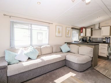 A living room with a sectional sofa and cushions next to a kitchen area with cabinets and appliances at Hazell Thorne Hideaway in Fritton