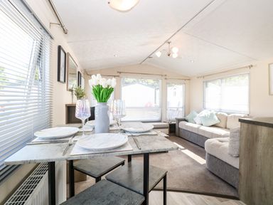 A dining table with plates and glasses next to a living area with sofas and large windows at Hazell Thorne Hideaway in Fritton