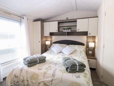 A bedroom with a bed with floral bedspread two white pillows folded towels and built in cabinets at Hazell Thorne Hideaway in Fritton
