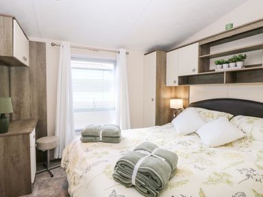 A bedroom with a bed with folded towels and white pillows next to a window with white curtains at Hazell Thorne Hideaway in Fritton