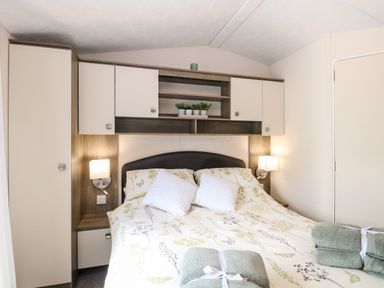 A bedroom with a double bed pillows and folded towels with overhead cabinets and small plants at Hazell Thorne Hideaway in Fritton