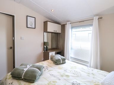 A bedroom with a bed holding folded towels a dressing table with a lamp and a window with curtains at Hazell Thorne Hideaway in Fritton