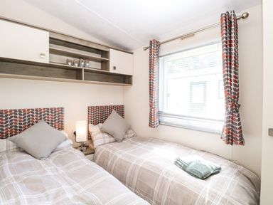 A bedroom with two single beds a window with patterned curtains and shelves above the beds at Hazell Thorne Hideaway in Fritton