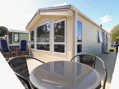 An outdoor patio area with a glass table and wicker chairs next to a beige mobile home at Hazell Thorne Hideaway in Fritton