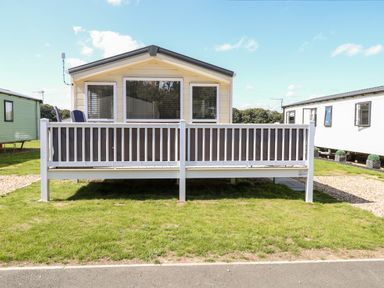 A beige mobile home with a white railing and deck chairs on the porch at Hazell Thorne Hideaway in Fritton