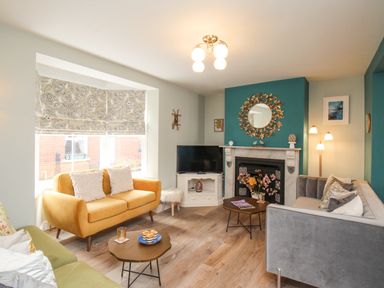 A living room with a yellow sofa a grey sofa a green chair a fireplace with a round mirror and a television at Bay Cottage in Weymouth